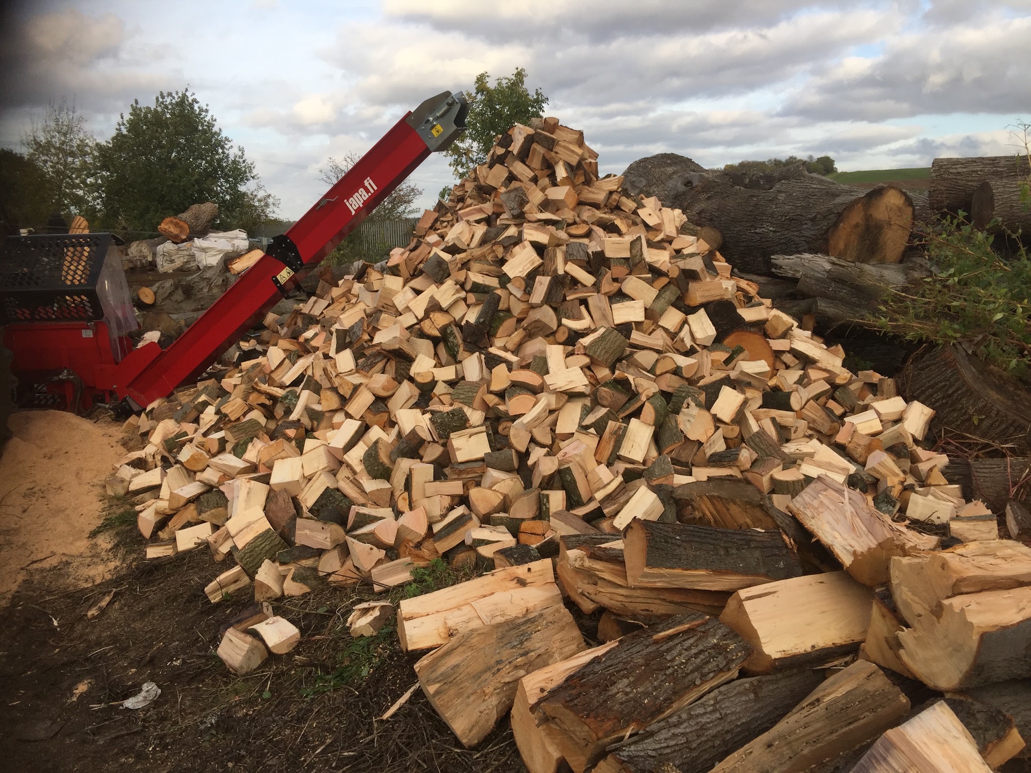 A big pile of freshly split logs beside our red firewood processor